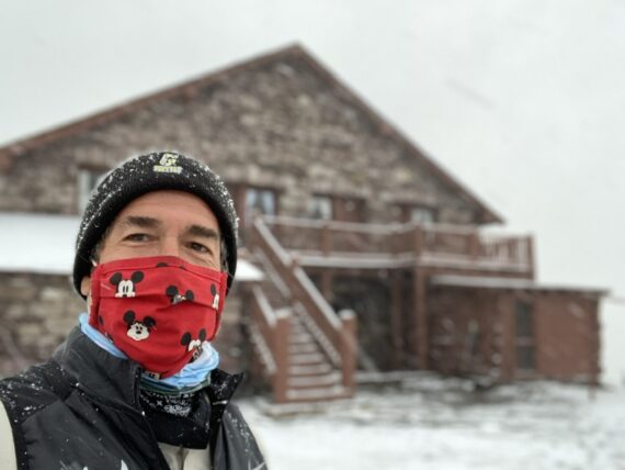 Man in a mask next to mountain  Chalet covered in snow