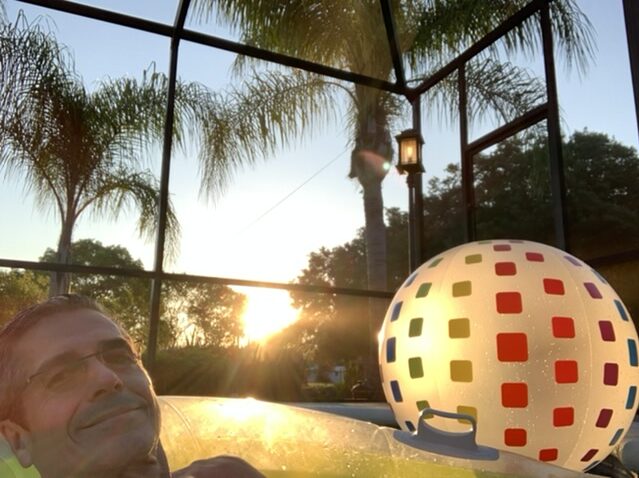 man in pool float as sun sets