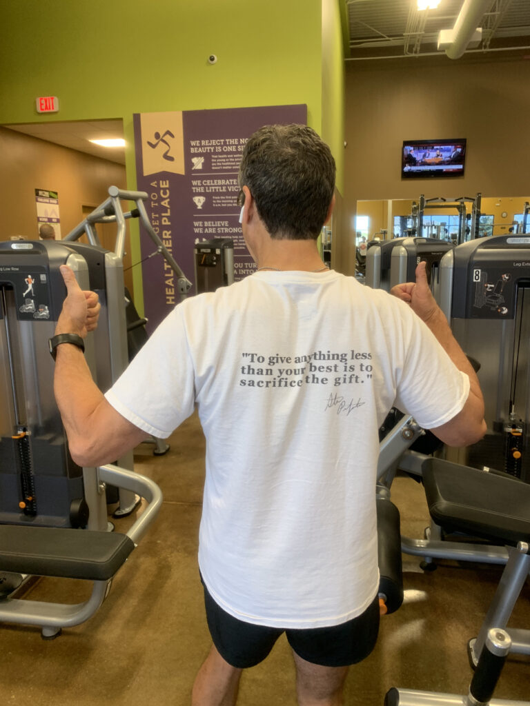 back side of a t-shirt being worn by a man in a gym