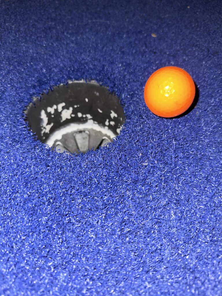 Orange golf ball next to hole