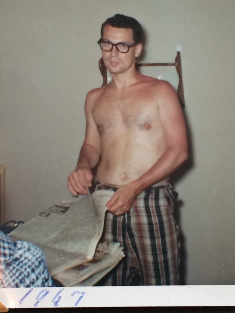 shirtless man in his dining room reading newspaper