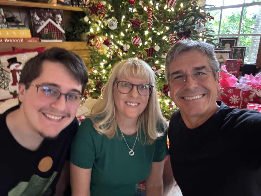 Three people sitting next to a Christmas tree